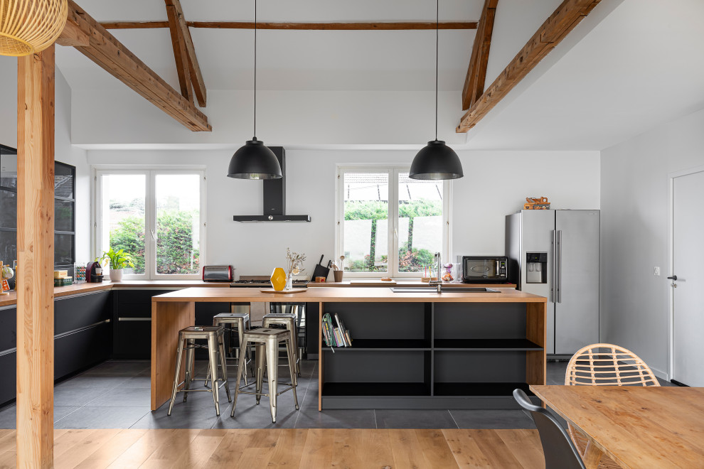 Inspiration for a contemporary l-shaped open plan kitchen in Lyon with a drop-in sink, flat-panel cabinets, black cabinets, wood benchtops, stainless steel appliances, with island, grey floor, brown benchtop, exposed beam and vaulted.