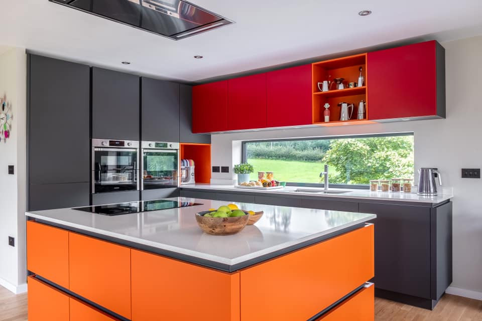 Mid-sized contemporary l-shaped eat-in kitchen in Gloucestershire with an integrated sink, flat-panel cabinets, orange cabinets, quartzite benchtops, stainless steel appliances, medium hardwood floors, with island and white benchtop.