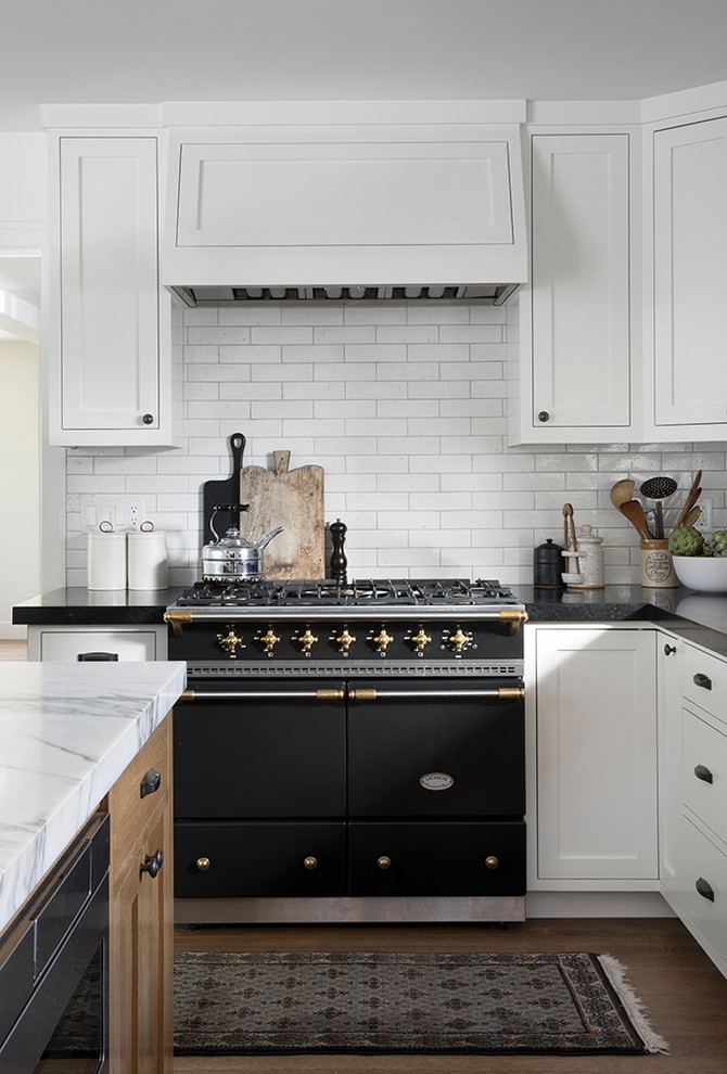 Mid-sized transitional l-shaped open plan kitchen in San Francisco with an undermount sink, beaded inset cabinets, white cabinets, marble benchtops, white splashback, cement tile splashback, stainless steel appliances, light hardwood floors, with island, brown floor and black benchtop.