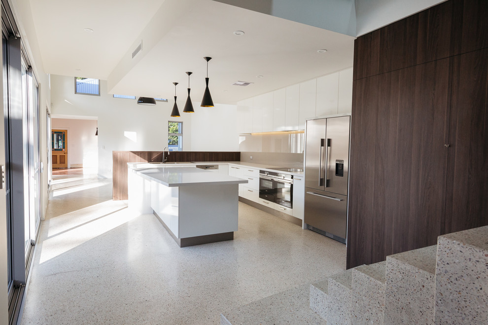 This is an example of a mid-sized modern l-shaped kitchen in Perth with a drop-in sink, white cabinets, solid surface benchtops, brown splashback, glass sheet splashback, stainless steel appliances, concrete floors and with island.