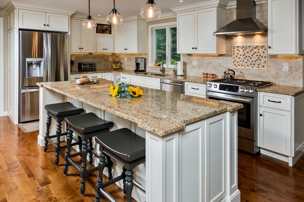Inspiration for a traditional l-shaped open plan kitchen in Portland Maine with an undermount sink, recessed-panel cabinets, white cabinets, beige splashback, stainless steel appliances, medium hardwood floors, with island, brown floor and beige benchtop.