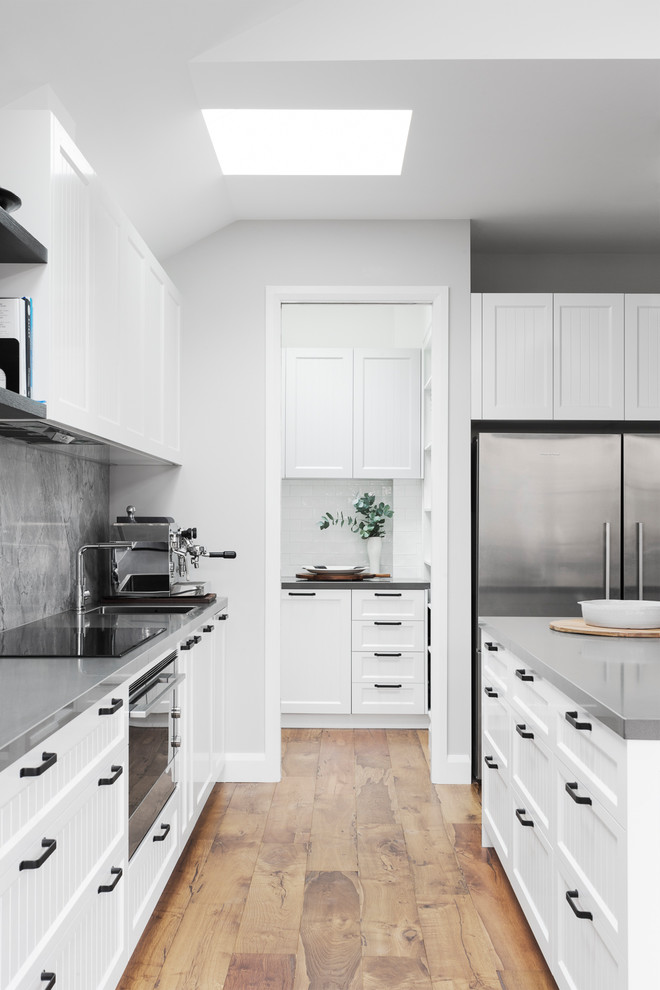 Design ideas for a large contemporary galley kitchen pantry in Melbourne with an undermount sink, shaker cabinets, white cabinets, quartz benchtops, grey splashback, stone slab splashback, stainless steel appliances, light hardwood floors, with island and grey benchtop.