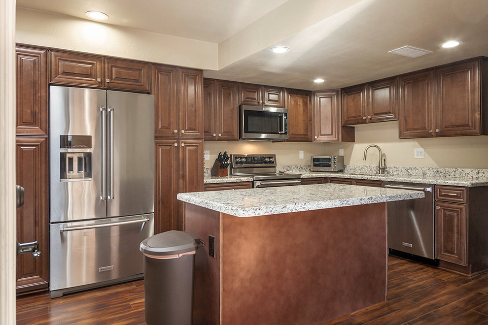 Mid-sized transitional l-shaped laminate floor and brown floor enclosed kitchen photo in Phoenix with an undermount sink, shaker cabinets, medium tone wood cabinets, granite countertops, multicolored backsplash, stone slab backsplash, stainless steel appliances and an island