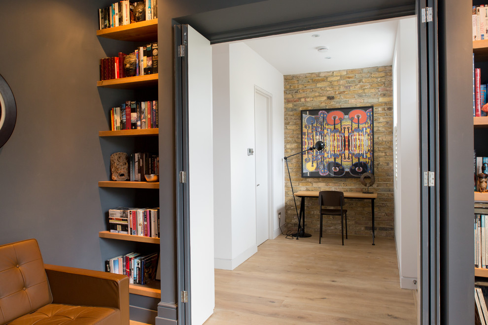 This is an example of a small contemporary home office in London with white walls, light hardwood floors, no fireplace and a freestanding desk.