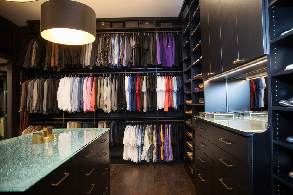 This is an example of a large modern gender-neutral walk-in wardrobe in New Orleans with flat-panel cabinets, black cabinets, dark hardwood floors and brown floor.