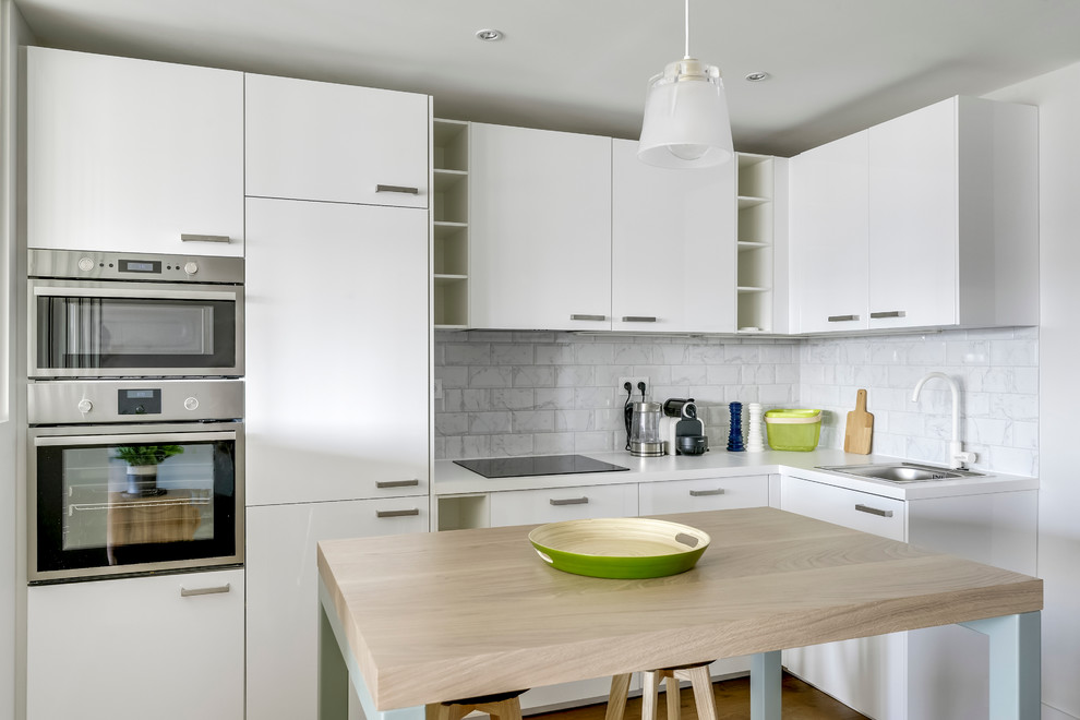 Design ideas for a mid-sized contemporary l-shaped open plan kitchen in Paris with white splashback, subway tile splashback, light hardwood floors, a single-bowl sink, flat-panel cabinets, white cabinets, laminate benchtops, stainless steel appliances and with island.