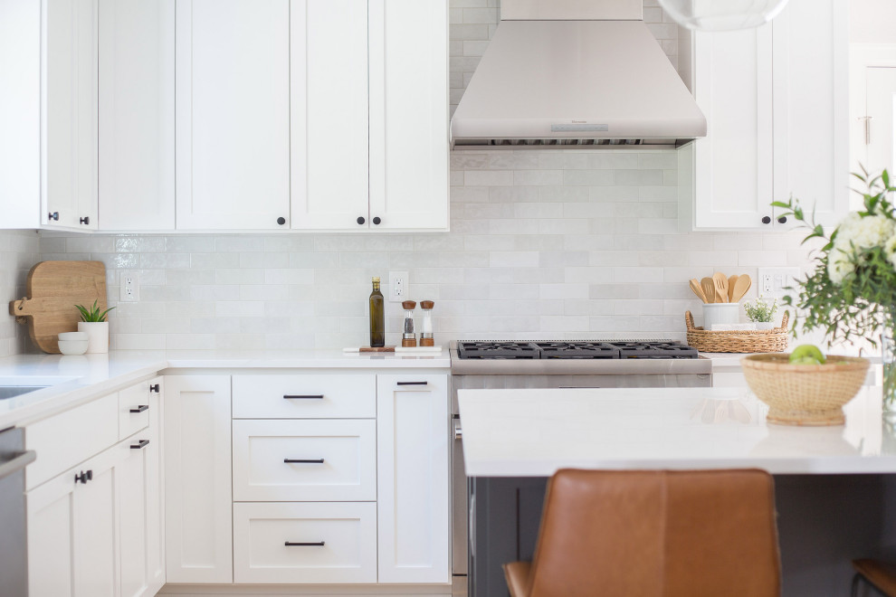 This is an example of a mid-sized country l-shaped eat-in kitchen in Seattle with an undermount sink, shaker cabinets, white cabinets, quartz benchtops, grey splashback, subway tile splashback, stainless steel appliances, light hardwood floors, with island, brown floor and white benchtop.