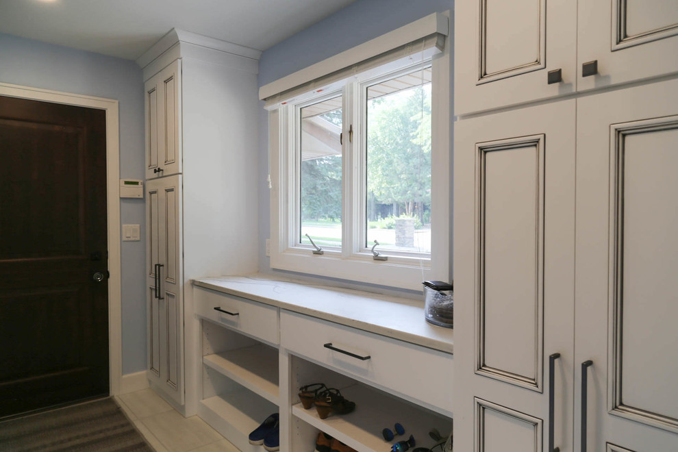 Photo of a mid-sized transitional mudroom in Other with blue walls, porcelain floors, a single front door, a medium wood front door and white floor.