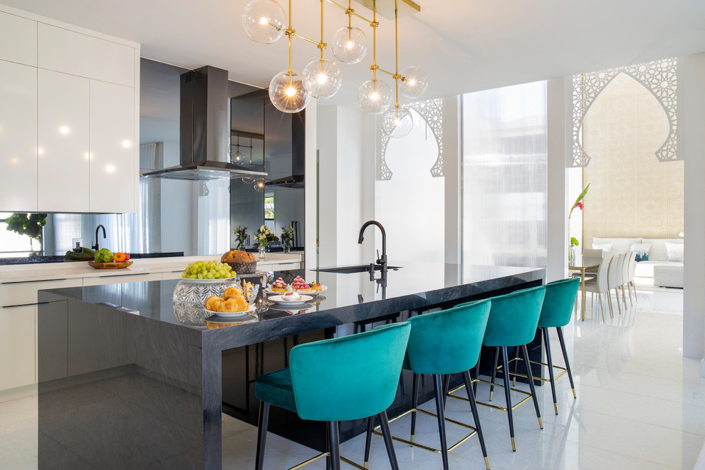 Large contemporary separate kitchen in Miami with an undermount sink, flat-panel cabinets, white cabinets, marble benchtops, grey splashback, mirror splashback, black appliances, marble floors, with island, white floor and black benchtop.