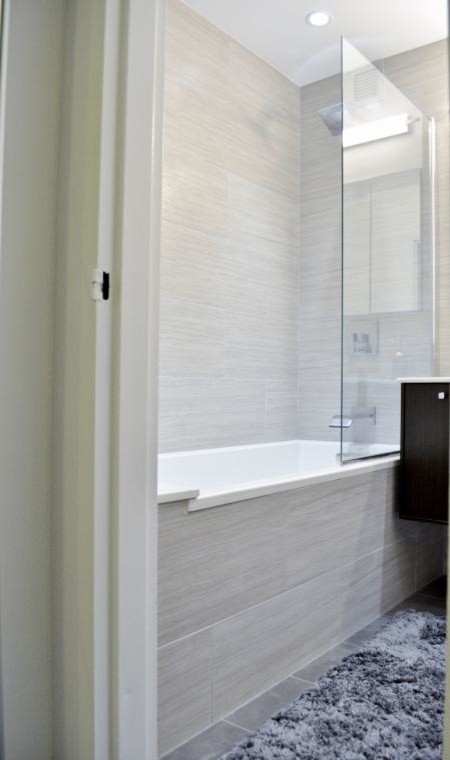 Inspiration for a mid-sized modern 3/4 bathroom in New York with flat-panel cabinets, dark wood cabinets, a drop-in tub, an alcove shower, gray tile, white walls, porcelain tile, solid surface benchtops, a two-piece toilet, porcelain floors and a wall-mount sink.