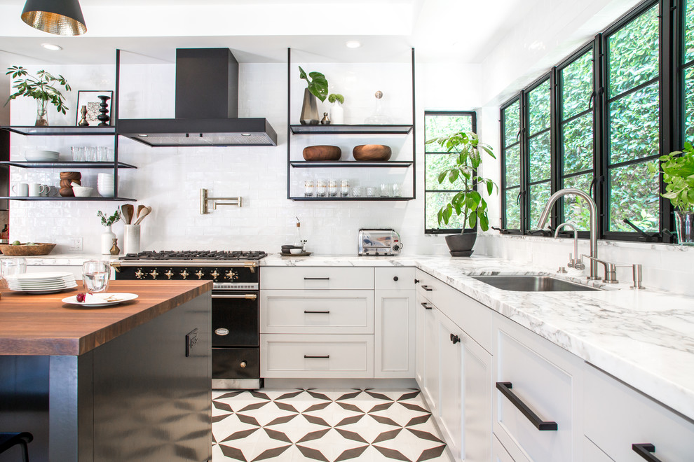 Photo of a transitional l-shaped kitchen in Los Angeles with an undermount sink, recessed-panel cabinets, white splashback, black appliances, cement tiles, with island and multi-coloured floor.