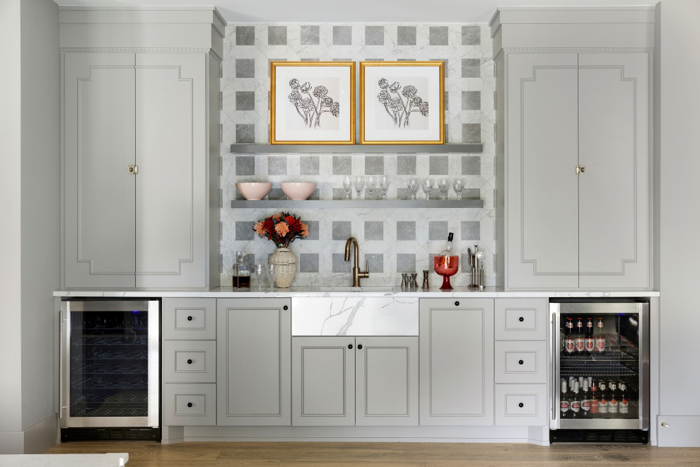 Inspiration for a country single-wall home bar in Minneapolis with recessed-panel cabinets, grey cabinets, grey splashback, medium hardwood floors, brown floor and white benchtop.