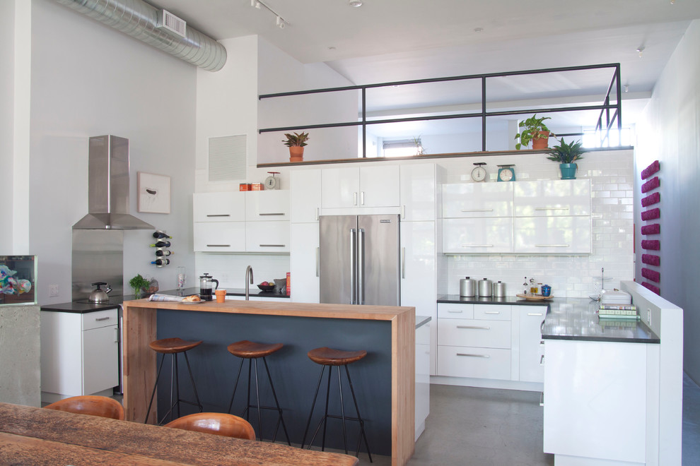 This is an example of a contemporary u-shaped eat-in kitchen in New York with flat-panel cabinets, white cabinets, white splashback, subway tile splashback, stainless steel appliances and with island.
