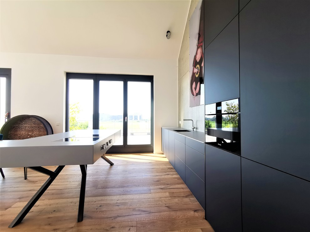 Offene, Große Moderne Küche mit Unterbauwaschbecken, flächenbündigen Schrankfronten, schwarzen Schränken, Edelstahl-Arbeitsplatte, schwarzen Elektrogeräten, Kücheninsel, braunem Boden und grauer Arbeitsplatte in München