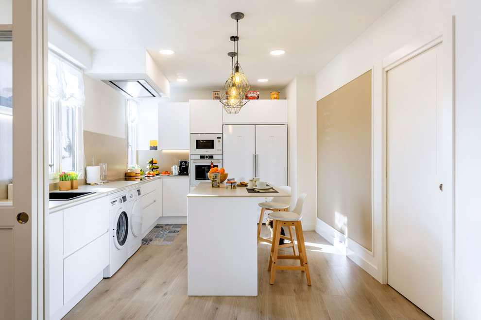 This is an example of a mid-sized contemporary l-shaped separate kitchen in Bilbao with flat-panel cabinets, white cabinets, beige splashback, white appliances, with island, light hardwood floors, beige floor and beige benchtop.