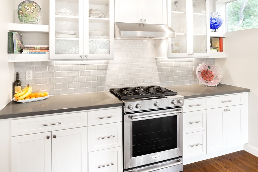 Eat-in kitchen - mid-sized transitional l-shaped medium tone wood floor eat-in kitchen idea with glass-front cabinets, white cabinets, quartz countertops, gray backsplash, ceramic backsplash and stainless steel appliances