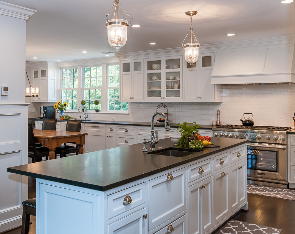 This is an example of a large traditional l-shaped open plan kitchen in DC Metro with a farmhouse sink, recessed-panel cabinets, white cabinets, quartz benchtops, white splashback, ceramic splashback, stainless steel appliances, dark hardwood floors, with island and brown floor.