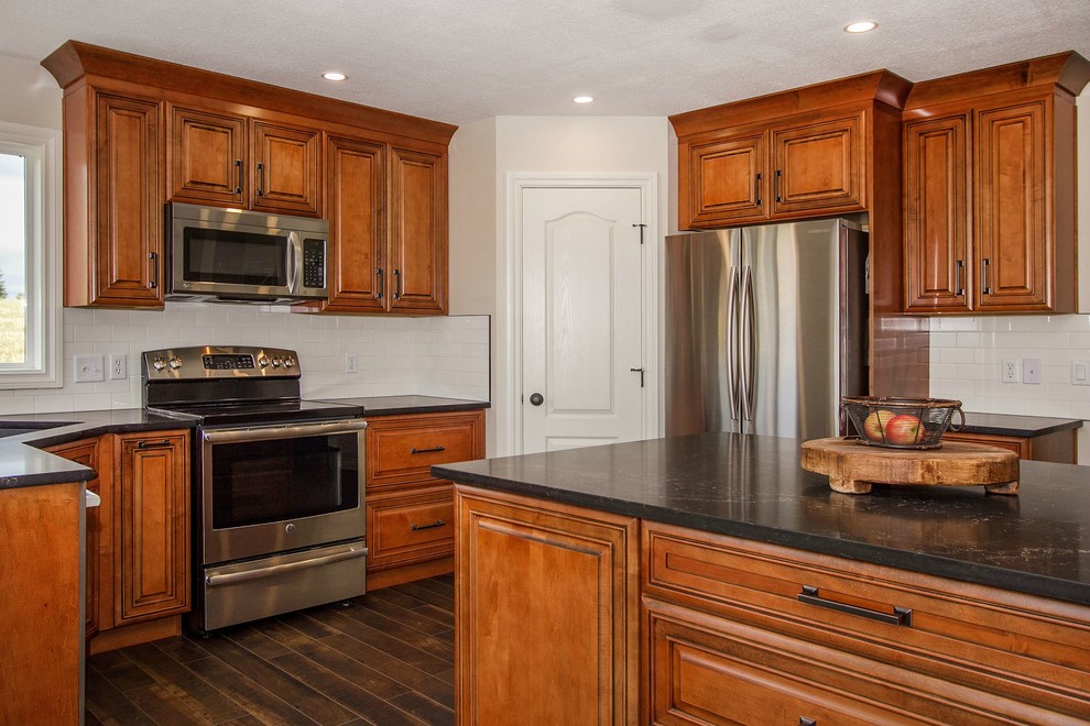 Mid-sized mountain style l-shaped laminate floor and black floor eat-in kitchen photo in Calgary with a drop-in sink, raised-panel cabinets, medium tone wood cabinets, quartzite countertops, white backsplash, ceramic backsplash, stainless steel appliances and an island