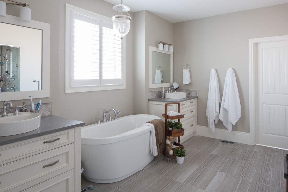 Photo of a large traditional master bathroom in Calgary with flat-panel cabinets, white cabinets, a freestanding tub, an alcove shower, gray tile, porcelain tile, grey walls, porcelain floors, a vessel sink and engineered quartz benchtops.