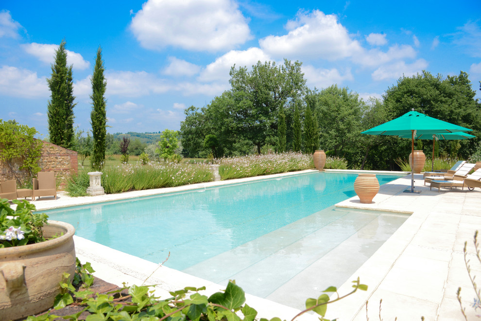 Large mediterranean backyard l-shaped lap pool in Toulouse with natural stone pavers.