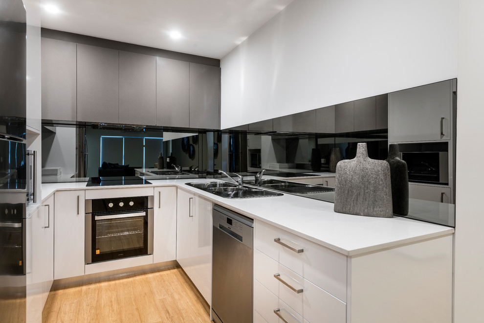 Small modern galley open plan kitchen in Perth with a double-bowl sink, recessed-panel cabinets, white cabinets, quartz benchtops, glass tile splashback, stainless steel appliances, light hardwood floors and no island.