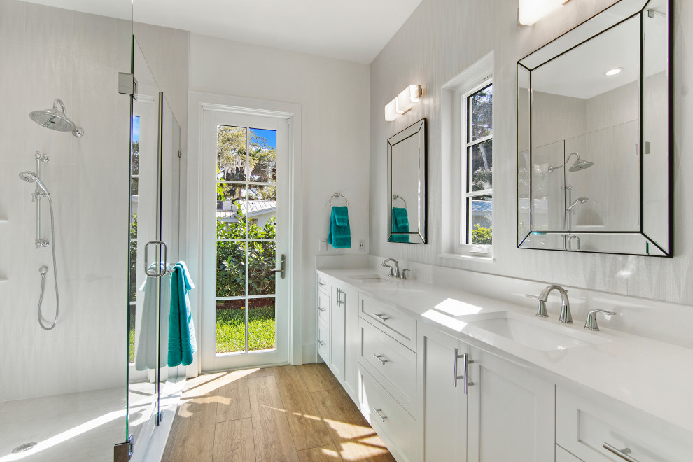 This is an example of a large beach style master wet room bathroom in San Diego with shaker cabinets, white cabinets, a one-piece toilet, white tile, porcelain tile, white walls, vinyl floors, an integrated sink, marble benchtops, beige floor, a hinged shower door, white benchtops, a shower seat, a double vanity, a built-in vanity and wallpaper.