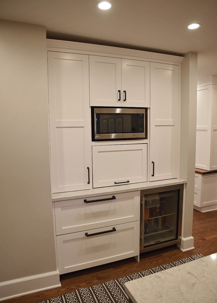 Example of a mid-sized transitional medium tone wood floor and brown floor enclosed kitchen design with an undermount sink, flat-panel cabinets, white cabinets, quartz countertops, white backsplash, ceramic backsplash, stainless steel appliances, an island and gray countertops