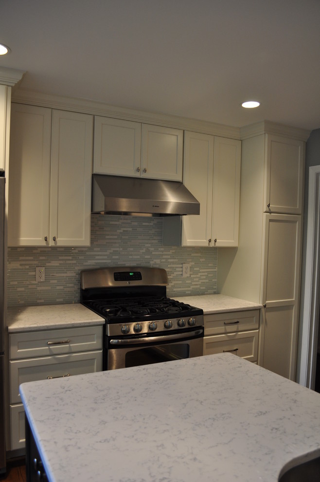 Large transitional u-shaped medium tone wood floor eat-in kitchen photo in DC Metro with a single-bowl sink, recessed-panel cabinets, white cabinets, marble countertops, blue backsplash, glass tile backsplash, stainless steel appliances and an island
