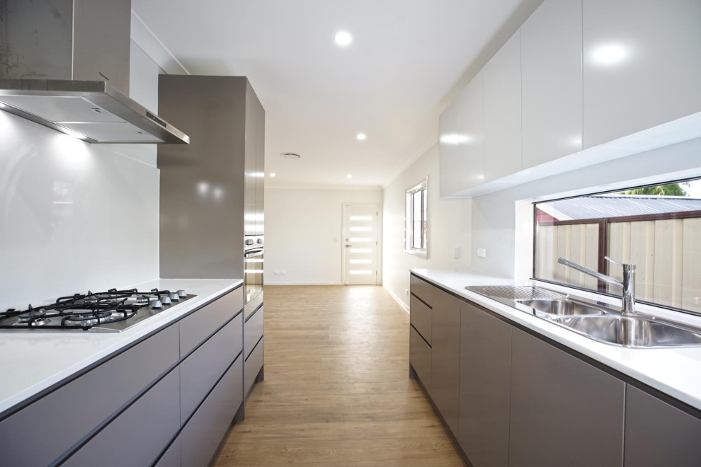 Inspiration for a mid-sized contemporary galley open plan kitchen in Sydney with a double-bowl sink, brown cabinets, yellow splashback, window splashback, stainless steel appliances, laminate floors, no island, brown floor and white benchtop.