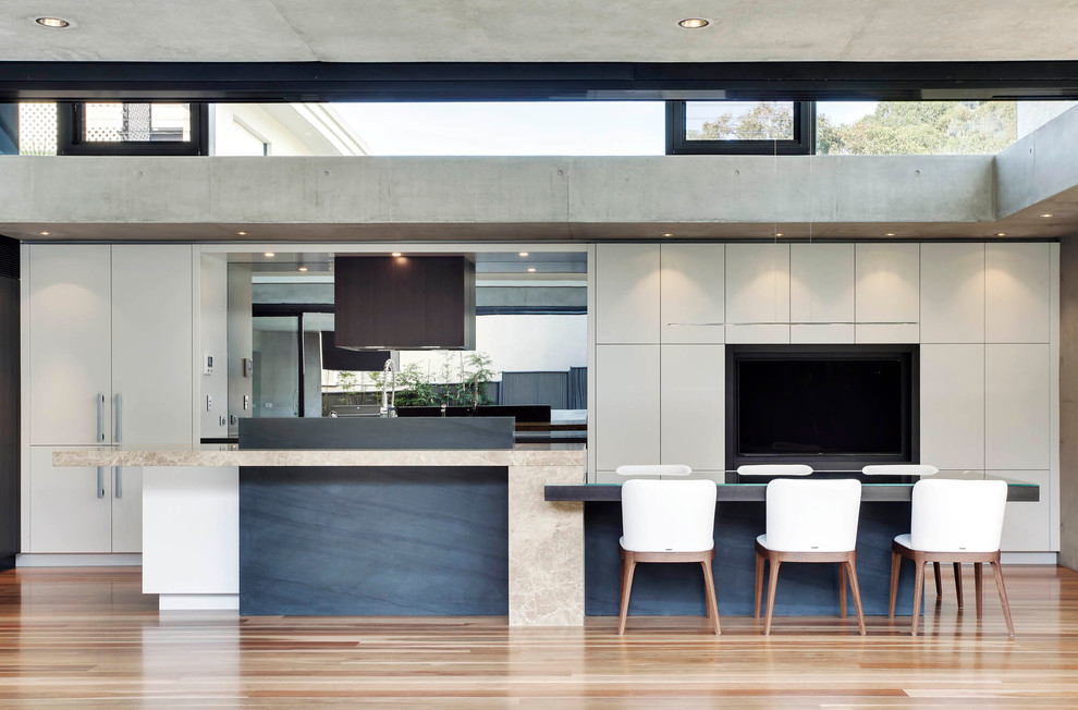 Design ideas for an expansive modern l-shaped eat-in kitchen in Sydney with an undermount sink, flat-panel cabinets, beige cabinets, marble benchtops, grey splashback, glass sheet splashback, black appliances, medium hardwood floors and with island.