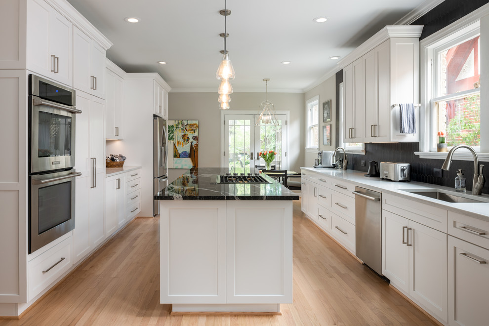 Inspiration for a transitional galley light wood floor and beige floor kitchen remodel in Dallas with an undermount sink, shaker cabinets, white cabinets, black backsplash, stainless steel appliances, an island and gray countertops