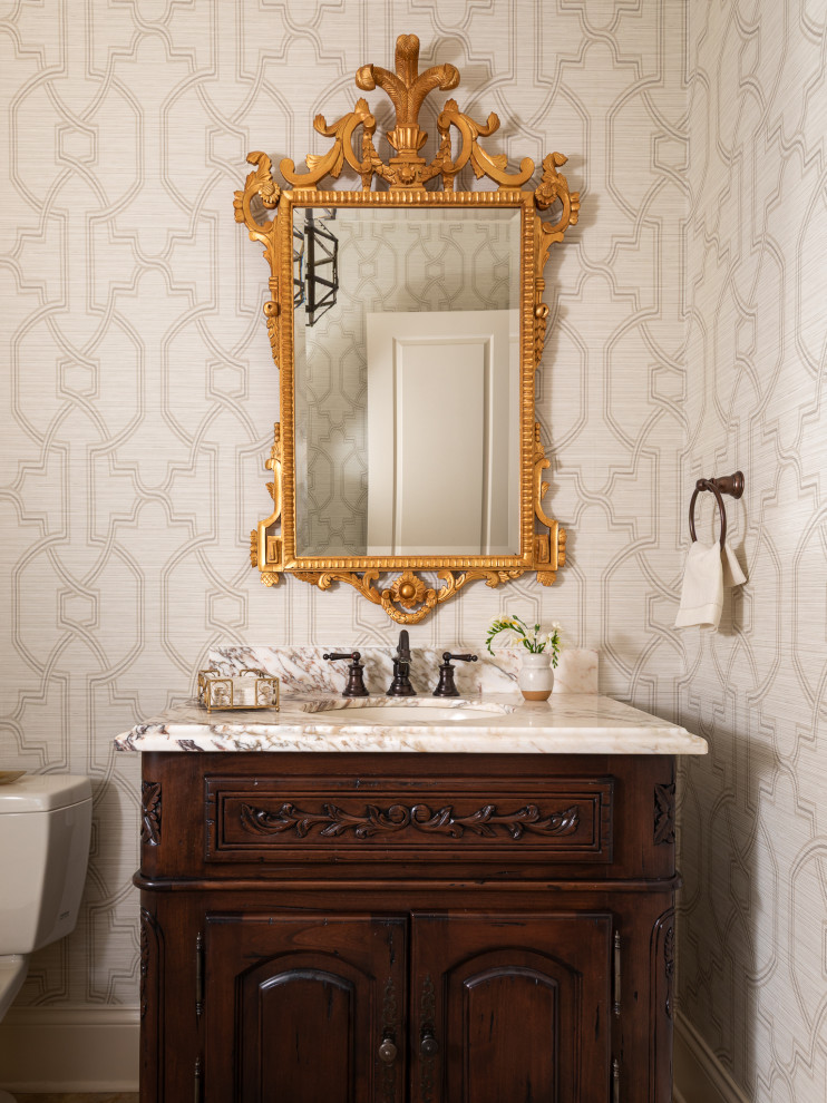 Inspiration for a mid-sized timeless travertine floor, beige floor and wallpaper powder room remodel in Indianapolis with furniture-like cabinets, dark wood cabinets, beige walls, an undermount sink, marble countertops, white countertops and a freestanding vanity