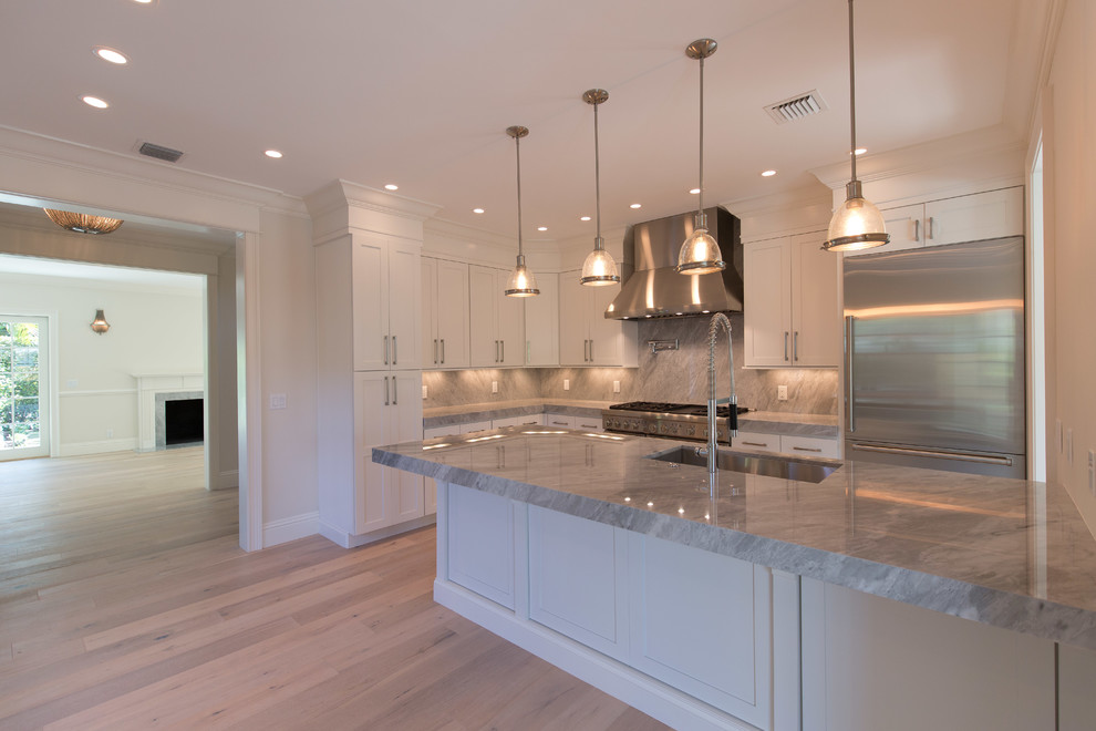 Example of a mid-sized transitional l-shaped light wood floor eat-in kitchen design in Miami with an undermount sink, recessed-panel cabinets, white cabinets, marble countertops, gray backsplash, stone slab backsplash, stainless steel appliances and an island
