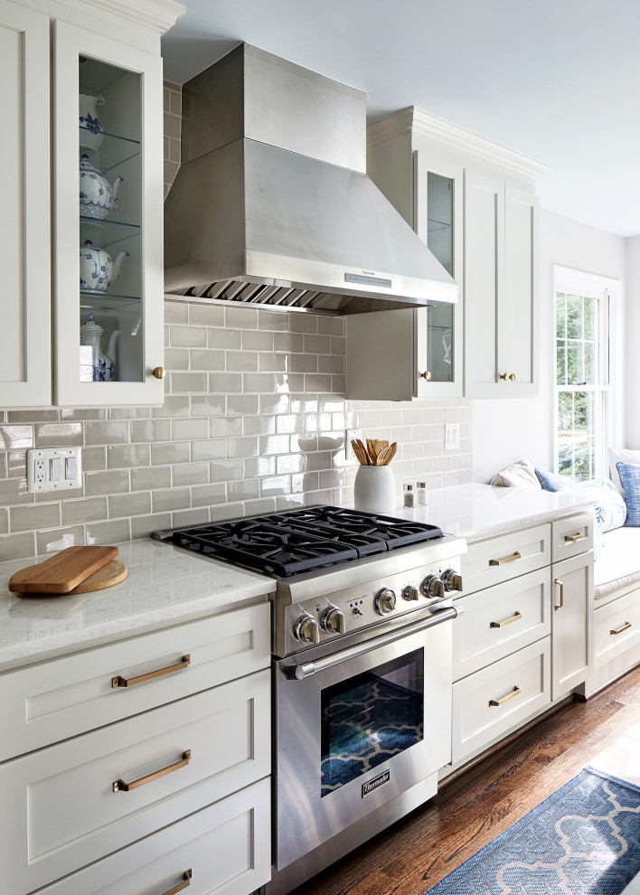 Inspiration for a mid-sized transitional eat-in kitchen in DC Metro with white cabinets, beige splashback, subway tile splashback, stainless steel appliances, medium hardwood floors, with island and white benchtop.