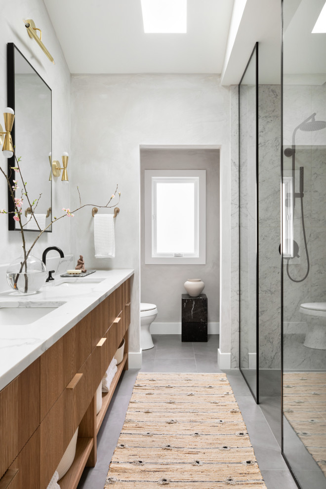 Design ideas for a mid-sized modern master bathroom in Chicago with furniture-like cabinets, medium wood cabinets, a curbless shower, a two-piece toilet, gray tile, porcelain tile, grey walls, porcelain floors, an undermount sink, engineered quartz benchtops, grey floor, an open shower, white benchtops, a laundry, a double vanity, a built-in vanity and vaulted.