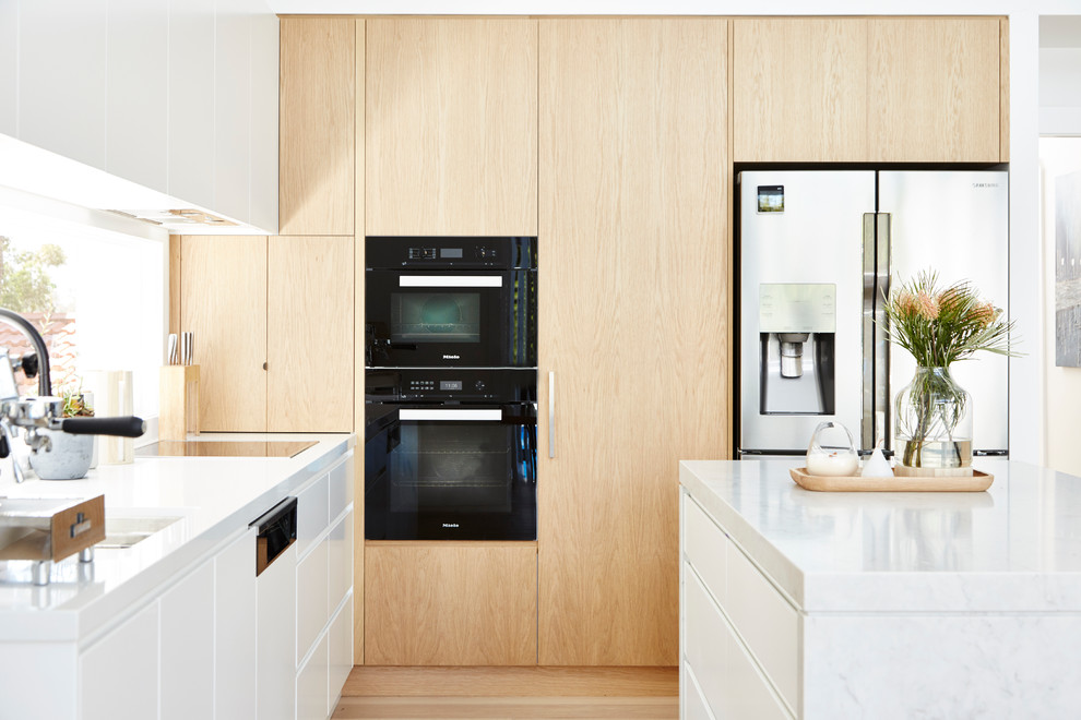 This is an example of a contemporary kitchen in Sydney with an undermount sink, flat-panel cabinets, light wood cabinets, marble benchtops, black appliances, light hardwood floors and multi-coloured benchtop.