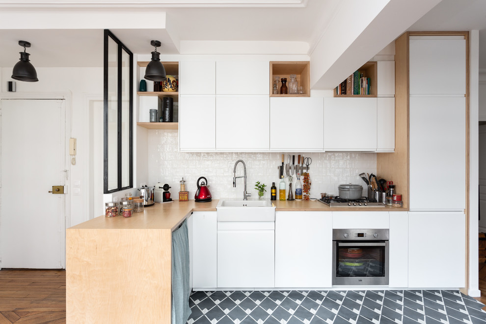 This is an example of a small scandinavian l-shaped eat-in kitchen in Paris with a farmhouse sink, flat-panel cabinets, white cabinets, wood benchtops, white splashback, stainless steel appliances, ceramic splashback, cement tiles, no island, grey floor and beige benchtop.
