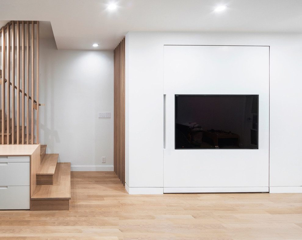 Photo of a large modern enclosed family room in New York with white walls, light hardwood floors, no fireplace and a concealed tv.