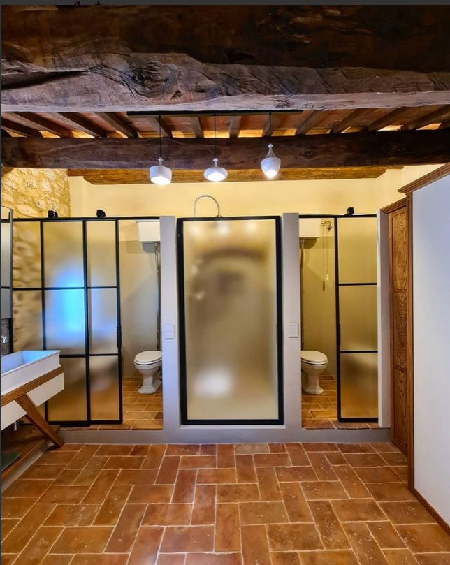 На фото: большая главная ванная комната в классическом стиле с открытыми фасадами, бежевыми фасадами, ванной на ножках, душем без бортиков, раздельным унитазом, бежевой плиткой, плиткой из известняка, бежевыми стенами, кирпичным полом, настольной раковиной, столешницей из дерева, коричневым полом, душем с распашными дверями, коричневой столешницей, тумбой под две раковины, встроенной тумбой, балками на потолке и кирпичными стенами с