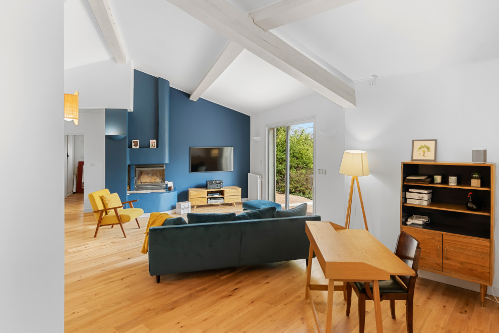 Foto di un grande soggiorno aperto con pareti blu, parquet chiaro, stufa a legna, TV a parete, pavimento beige e travi a vista