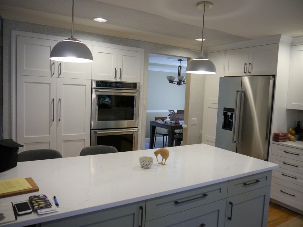 This is an example of a large transitional l-shaped eat-in kitchen in Seattle with an undermount sink, shaker cabinets, white cabinets, quartz benchtops, grey splashback, ceramic splashback, stainless steel appliances, light hardwood floors, with island, yellow floor and white benchtop.