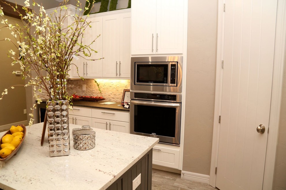 Example of a small transitional u-shaped light wood floor open concept kitchen design in Orange County with an undermount sink, louvered cabinets, white cabinets, solid surface countertops, beige backsplash, stone tile backsplash, stainless steel appliances and two islands