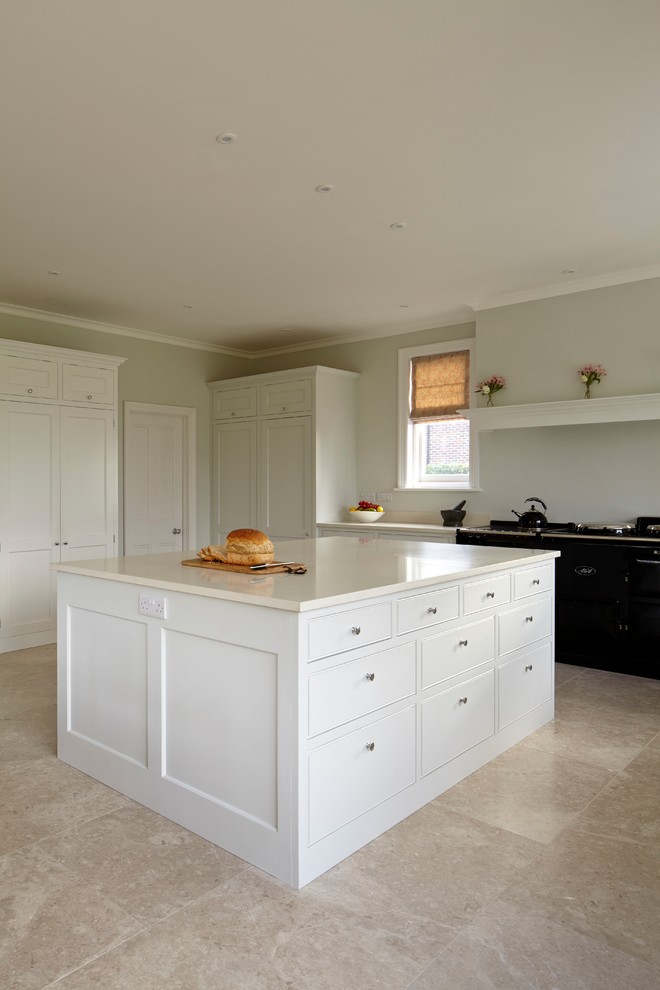Design ideas for a mid-sized traditional l-shaped open plan kitchen in Hampshire with a farmhouse sink, shaker cabinets, white cabinets, quartzite benchtops, black appliances, limestone floors, with island, beige floor and white benchtop.