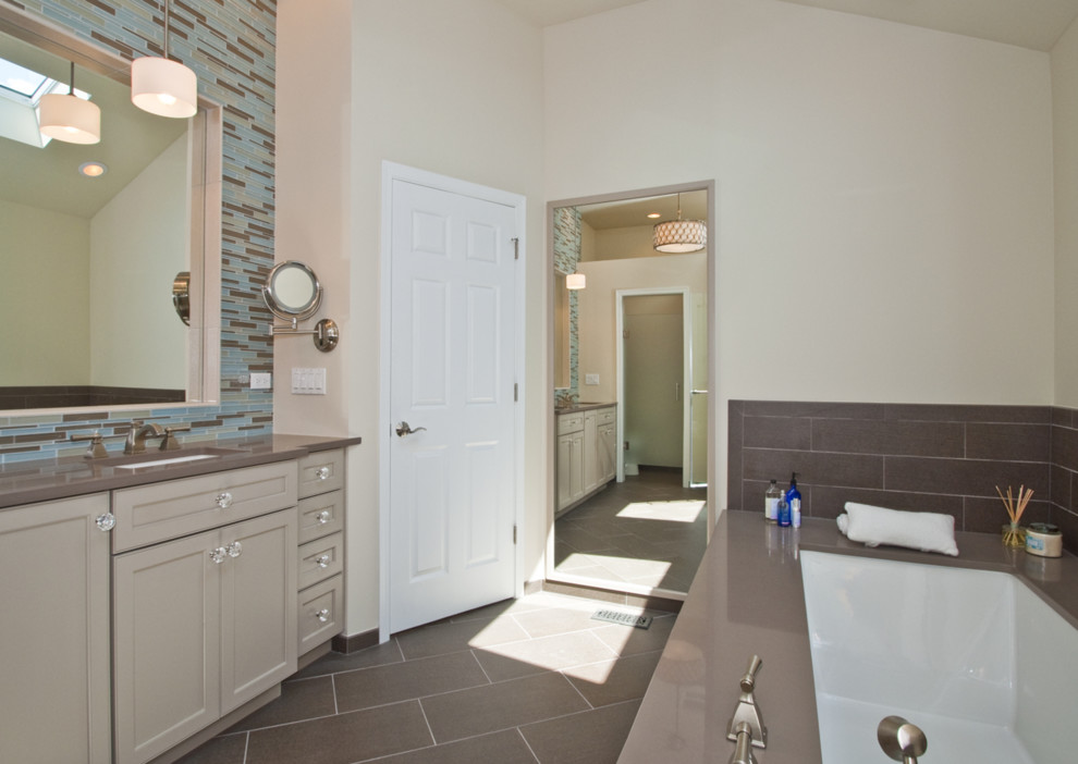 This is an example of a transitional bathroom in Chicago with an undermount sink, recessed-panel cabinets, white cabinets, engineered quartz benchtops, an undermount tub, a one-piece toilet, gray tile and porcelain tile.