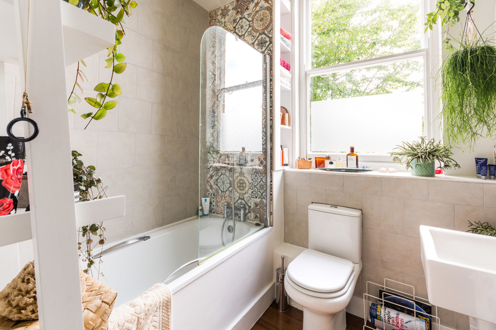 Mid-sized eclectic master bathroom in London with a drop-in tub, a shower/bathtub combo, dark hardwood floors, brown floor, a two-piece toilet, beige tile, multi-coloured tile, multi-coloured walls and an open shower.