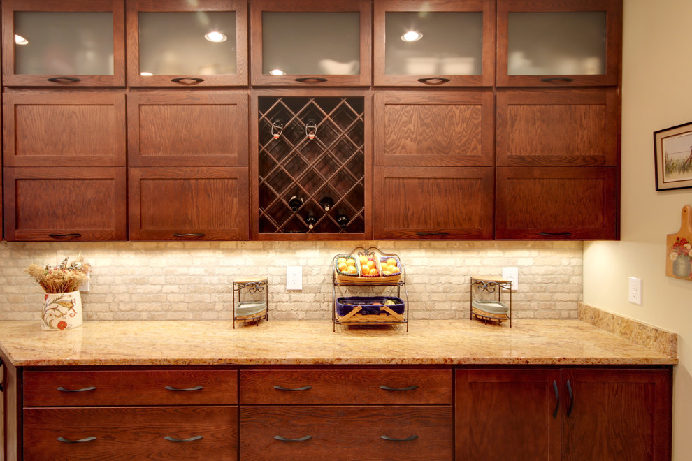 Transitional eat-in kitchen photo in Miami with an undermount sink, shaker cabinets, brown cabinets, granite countertops, beige backsplash, stone tile backsplash and stainless steel appliances