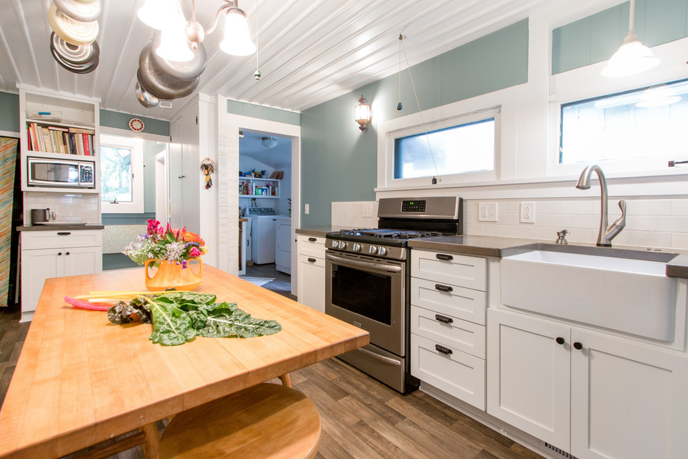 Photo of a small country galley separate kitchen in Milwaukee with a farmhouse sink, flat-panel cabinets, white cabinets, quartz benchtops, white splashback, ceramic splashback, stainless steel appliances, medium hardwood floors and no island.