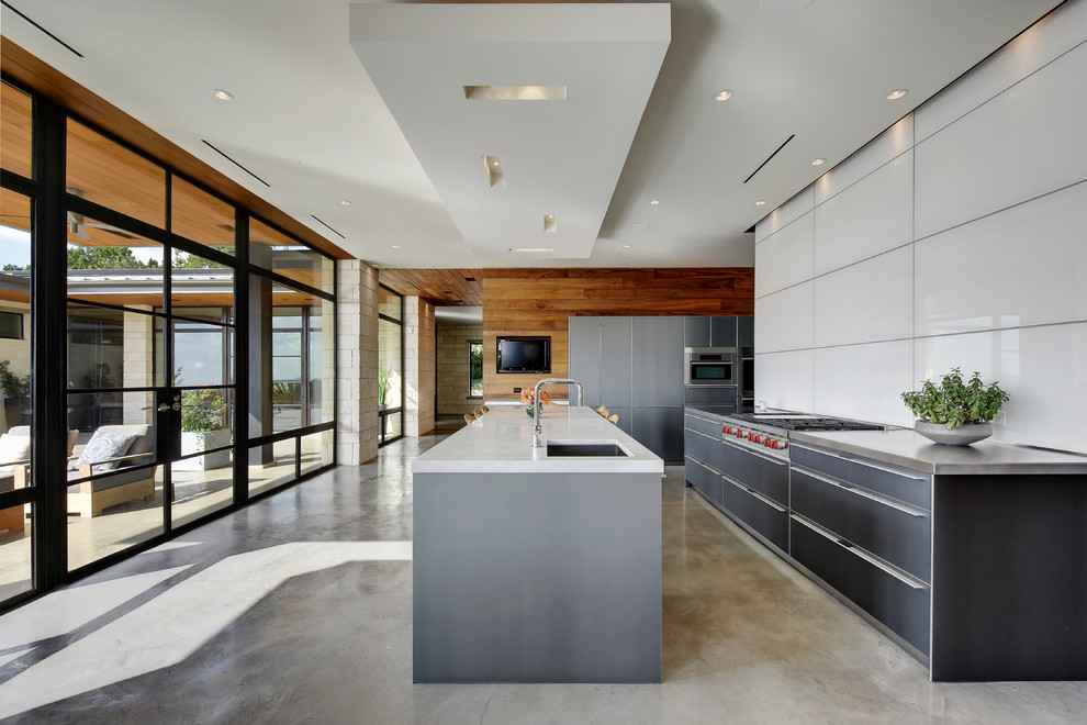 Photo of a contemporary l-shaped kitchen in Austin with an undermount sink, flat-panel cabinets, grey cabinets, white splashback, glass sheet splashback, stainless steel appliances, concrete floors and with island.