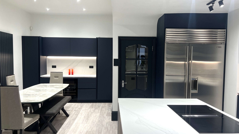Mid-sized modern l-shaped eat-in kitchen in London with a drop-in sink, flat-panel cabinets, blue cabinets, quartzite benchtops, white splashback, black appliances, porcelain floors, with island, grey floor, white benchtop and exposed beam.