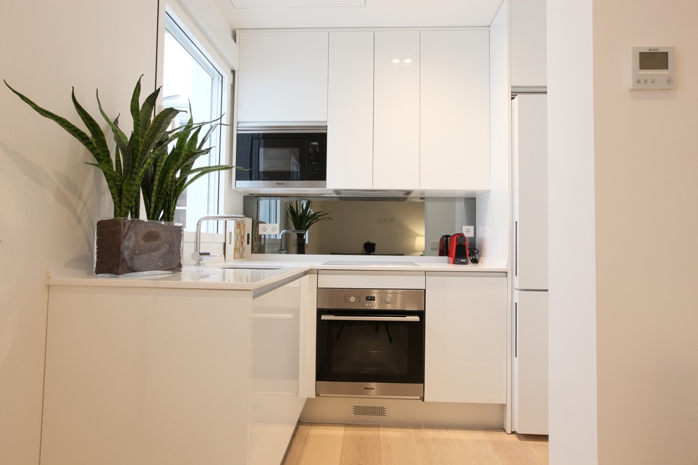 This is an example of a small scandinavian l-shaped open plan kitchen in Madrid with an undermount sink, flat-panel cabinets, white cabinets, quartz benchtops, grey splashback, window splashback, stainless steel appliances, light hardwood floors, no island, beige floor and white benchtop.